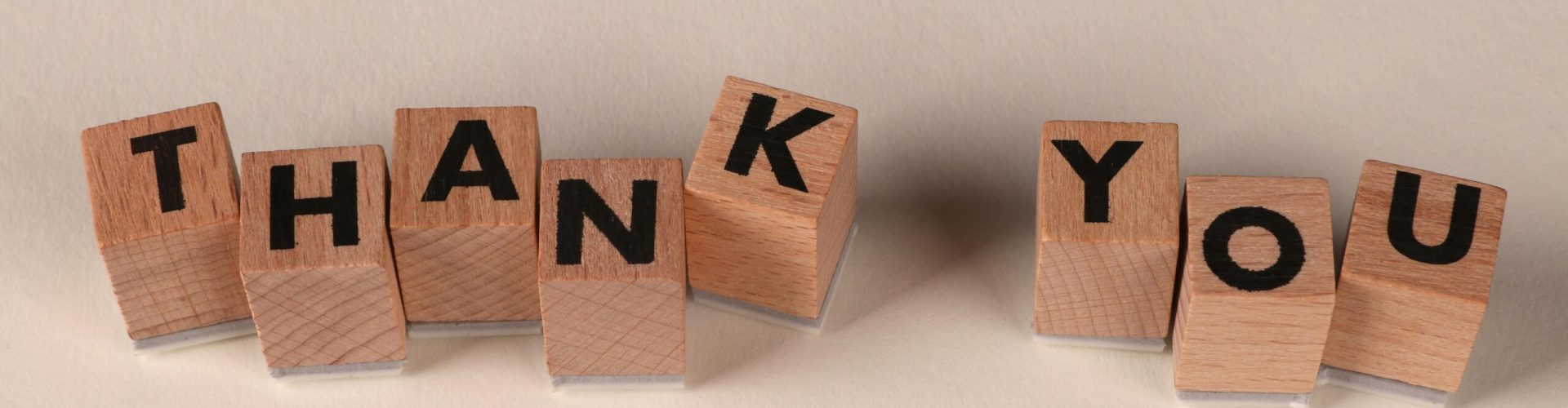 Wooden blocks spell 'THANK YOU' on a soft beige background, expressing gratitude.